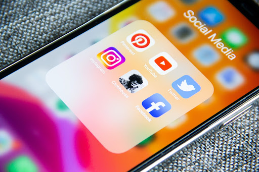 Close up image of an iphone showing a selection of social media apps including Pinterest, YouTube, Twitter, Instagram, Clubhouse, and Facebook.