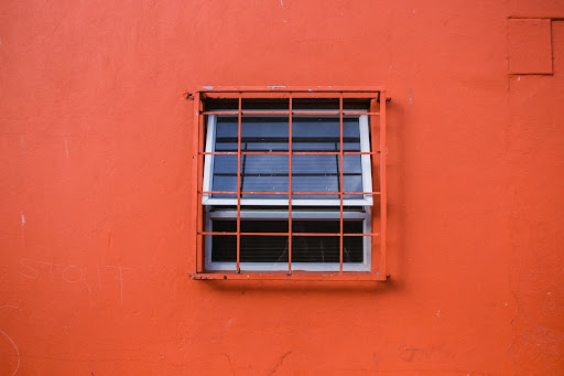 A window covered with a metal grate on a bright orange wall.