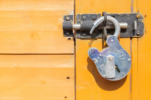 A large padlock securing the door on a yellow shed.